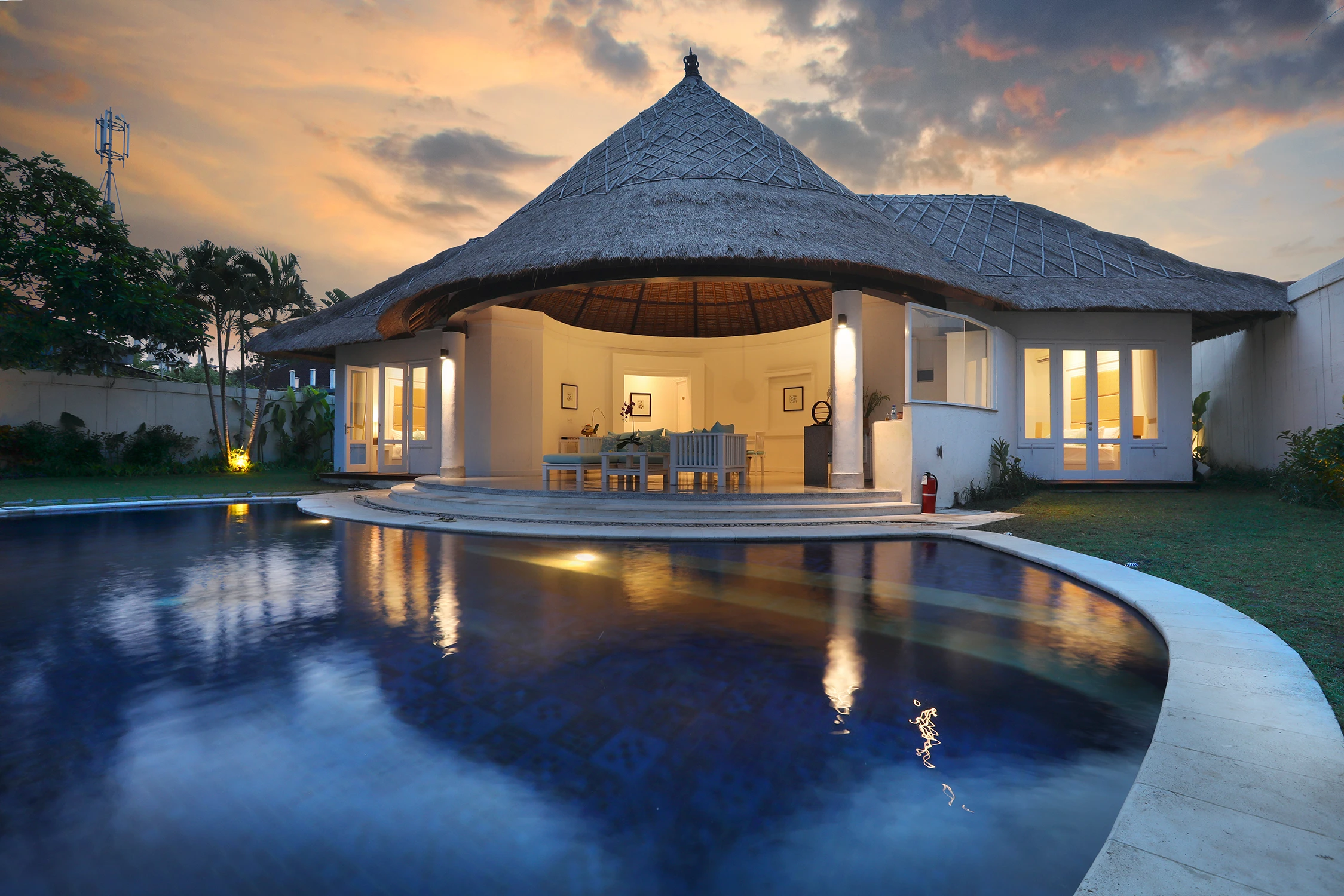 Роскошная вилла Умалас на Бали с персональным бассейном, лаундж-зоной и традиционной соломенной крышей в вечерней подсветке.
